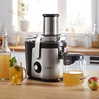 Bosch juicer i sølv presser æblejuice med glas og frisk frugt på køkkenbord